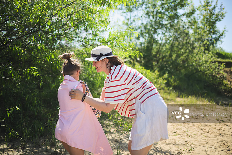 在海滩上，妈妈温柔地拥抱着女儿，用毛巾把她包裹起来，享受着炎热的夏天。图片素材