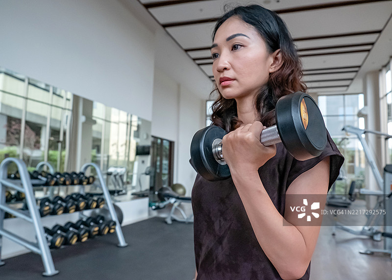 亚洲女性举哑铃进行上半身训练图片素材