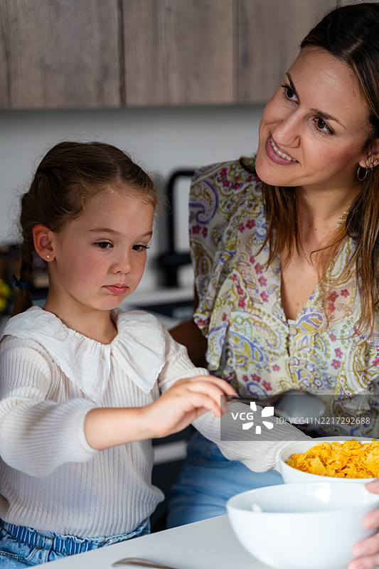 母亲在厨房里把玉米片倒入女儿的碗中图片素材