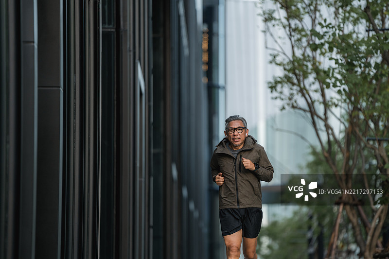 在公共公园里慢跑的老年男子，戴着无线耳机听音乐图片素材