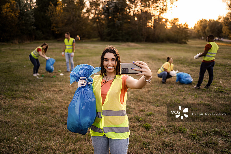 年轻女性在公园与志愿者一起捡垃圾时自拍图片素材