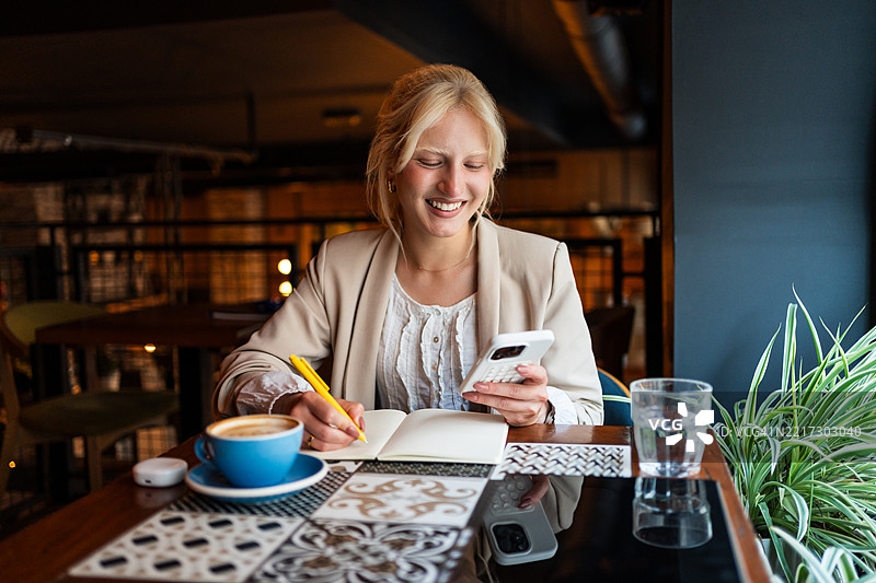 在咖啡馆远程工作的女商人，记笔记并使用计算器应用程序图片素材