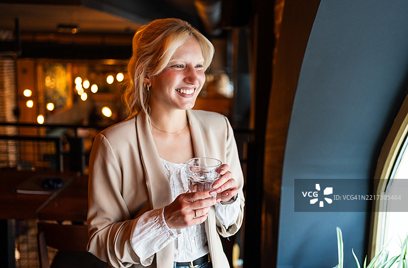 年轻的金发女性在餐厅里微笑着喝水图片素材
