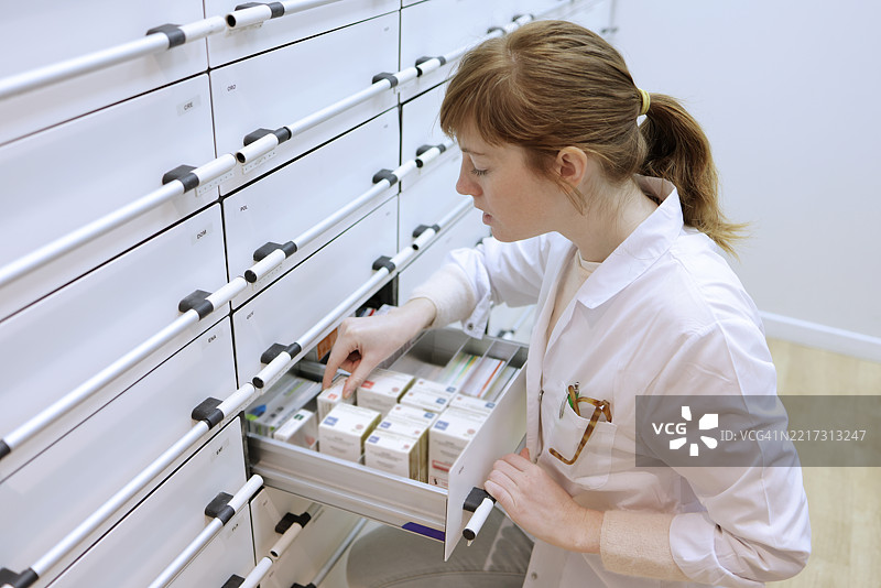 一位在药店工作的女性，将药品放入储藏室的抽屉中图片素材