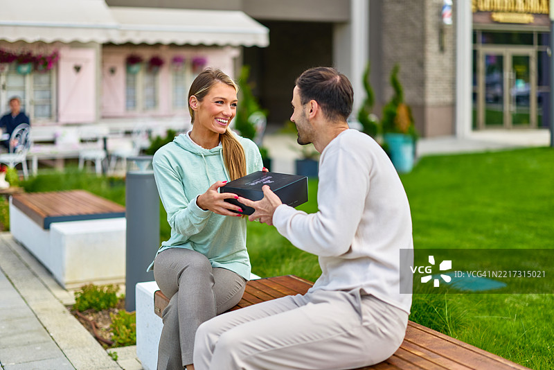 年轻恩爱情侣坐在长椅上互赠礼物图片素材