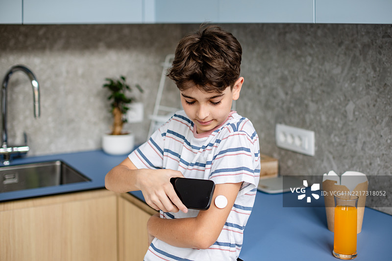 年轻男孩在家里的厨房环境中使用连续血糖监测仪管理1型糖尿病图片素材