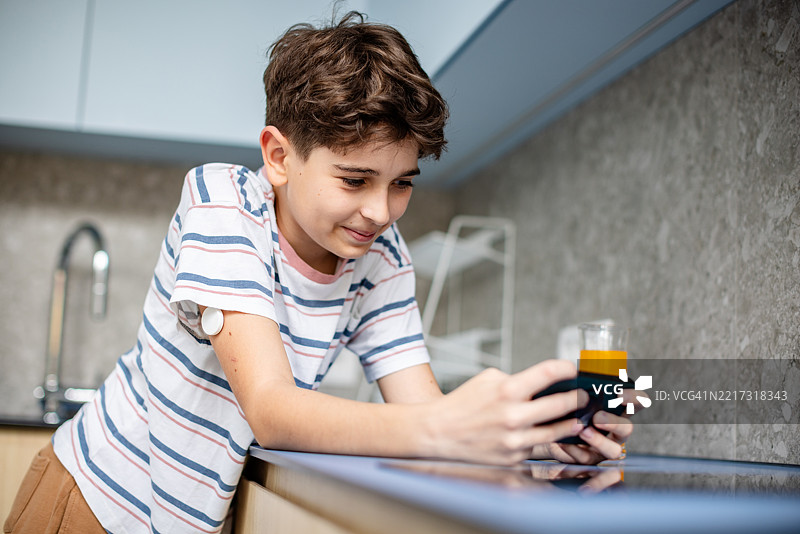 年轻男孩在温馨的家庭厨房环境中使用血糖监测仪和果汁管理1型糖尿病图片素材