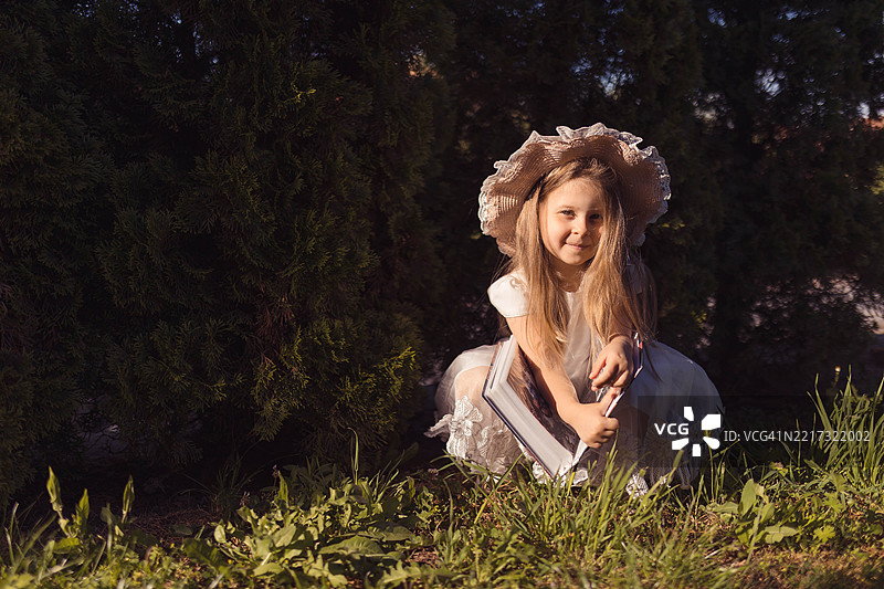 漂亮的小金发女孩坐在草地上，翻看家庭相册。图片素材