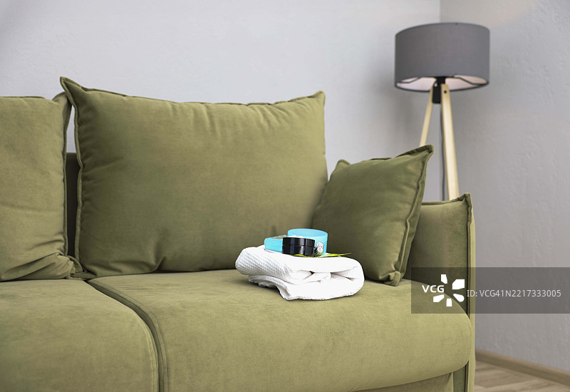 折叠的白色毛巾上放着水疗护肤产品， resting on soft green sofa with large cushions，舒适宜人。图片素材