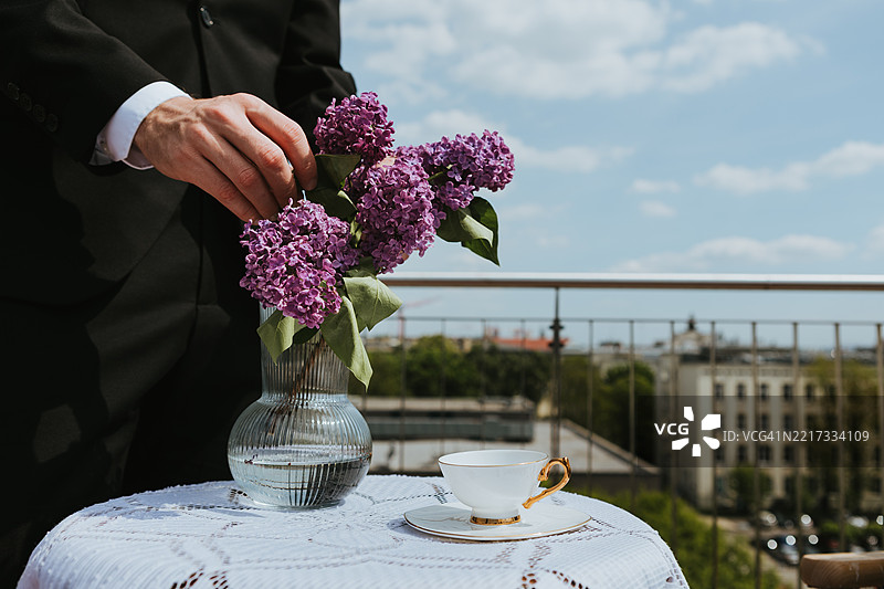 男人的中部拿着花和花瓶，桌子上对着天空图片素材