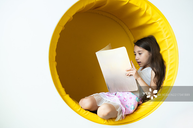 小女孩坐在黄色扶手椅上阅读一本书图片素材
