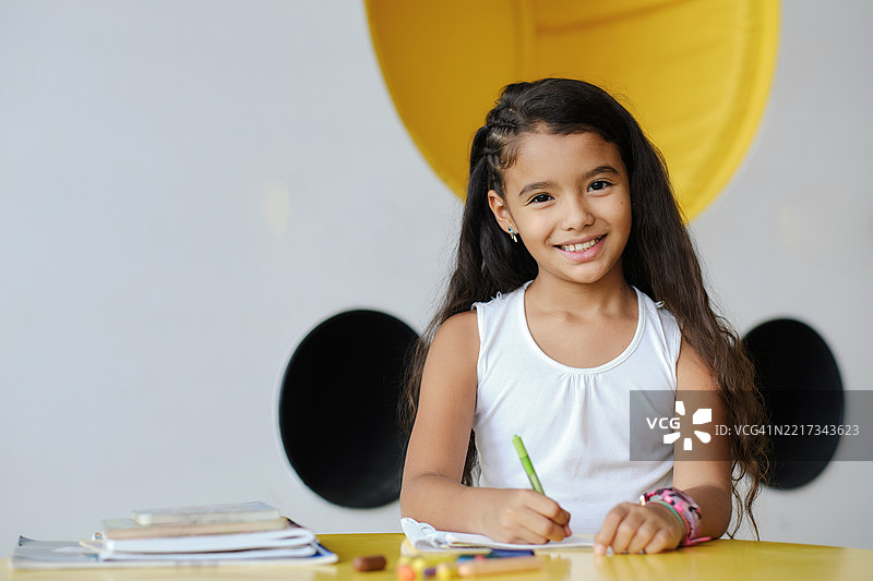 微笑的小学生在色彩缤纷的教室里桌子上画画图片素材