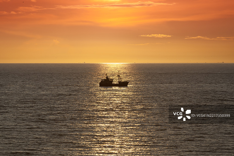 在舍夫宁根北海海岸的日落时分，拖网渔船驶过。图片素材