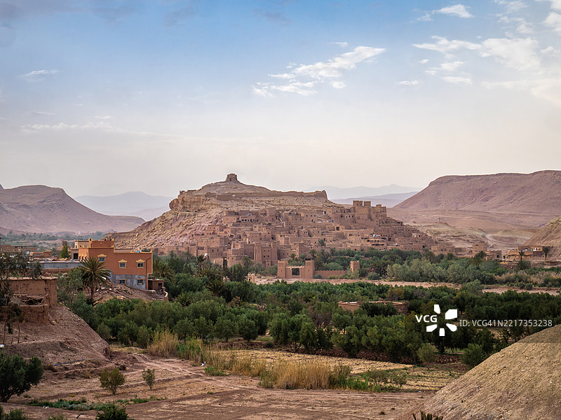 日落时分,远距离鸟瞰阿伊特·本哈杜(Ait Benhaddou)古堡,著名的由泥土和夯土建成的柏柏尔人防御村庄,前景是一个绿洲,联合国教科文组织世界遗产 - 乌尼拉谷 - 瓦尔扎扎特省 - 摩洛哥。图片素材