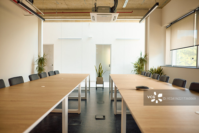 现代会议室内有两张长桌和准备好的椅子，适合商务会议。图片素材