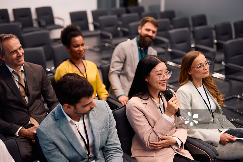 年轻女商人在会议上使用麦克风发言，坐在观众席中。图片素材
