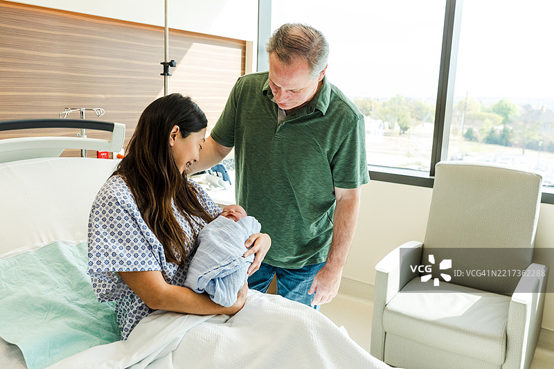 父母在医院病房里欣赏他们的新生儿图片素材