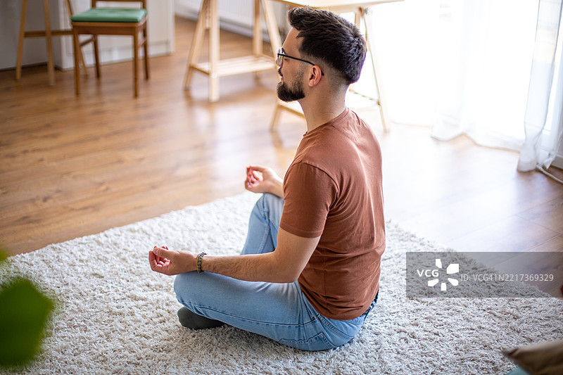 年轻男子在家中坐在地毯上以莲花坐姿冥想图片素材