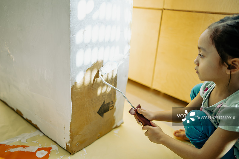 小女孩用滚筒给纸板涂白漆图片素材