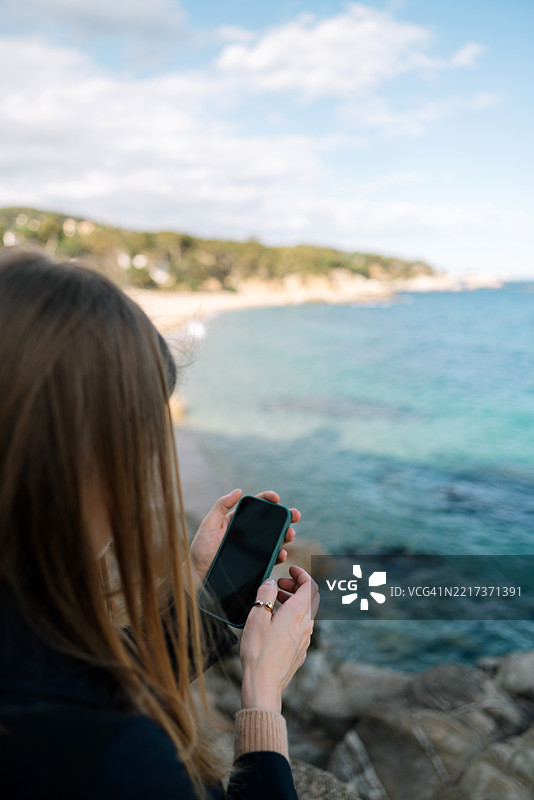 女人背对着海洋拍照，天空在背景中。图片素材