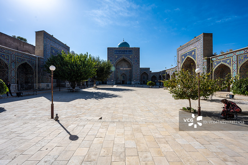 在雷吉斯坦广场的谢尔-多尔神学院庭院，阳光明媚，一位孤独的身影坐在阴凉处。图片素材