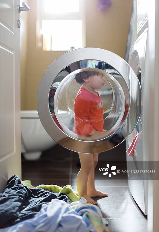 孩子在明亮的洗衣房里从洗衣机里偷看图片素材