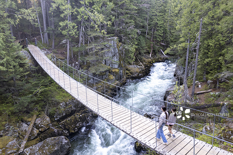 年轻女孩在河上走过悬索桥的鸟瞰图图片素材