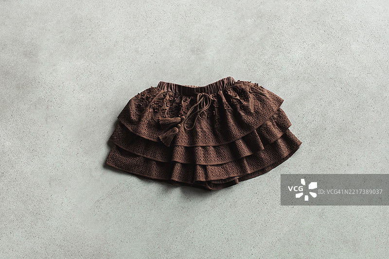 优雅的分层棕色裙子，带有穿孔细节，背景为混凝土。图片素材