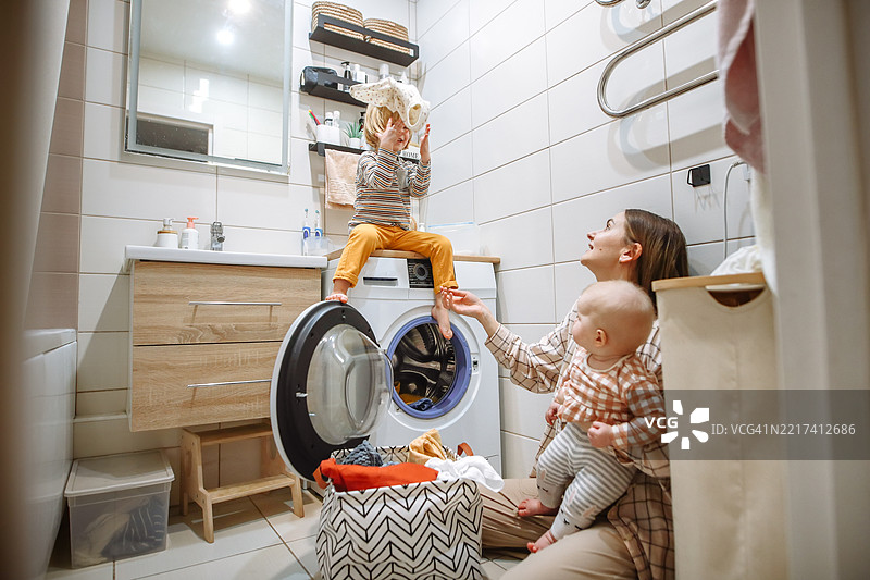 妈妈在狭小的家用浴室里一边洗衣服一边照顾两个小孩图片素材