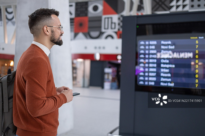 机场航站楼：年轻男子在查看到达和出发信息显示屏，寻找他的航班图片素材