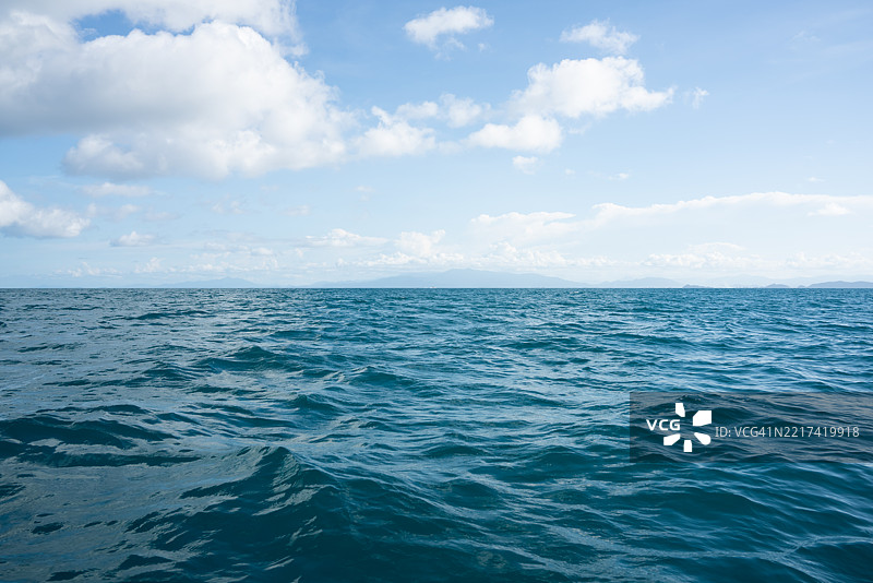 阳光明媚的日子里，平静的海面和远处的岛屿风景图片素材