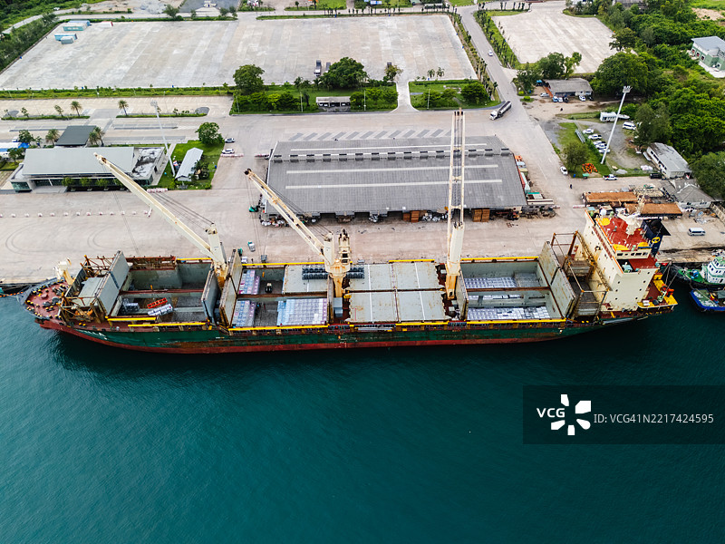 从上方俯视停靠在商业港口的货船，起重机正在卸载各种货物和集装箱。图片素材