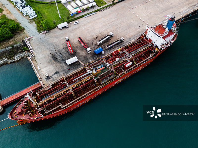 油轮停靠在混凝土港口的鸟瞰图，燃油卡车通过连接的软管装卸石油。图片素材