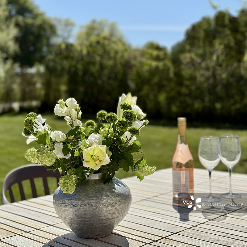花瓶里的花朵特写，放在花园桌子上，旁边有一瓶玫瑰酒和两个酒杯图片素材