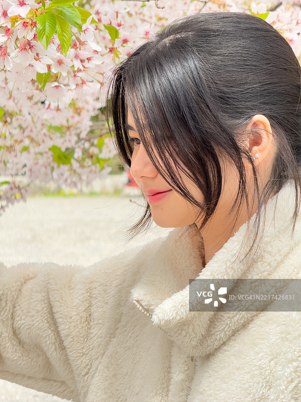 微笑的年轻女性肖像，穿着抓绒衣，站在盛开的樱花树前，地点：日本长野县下高井地区图片素材
