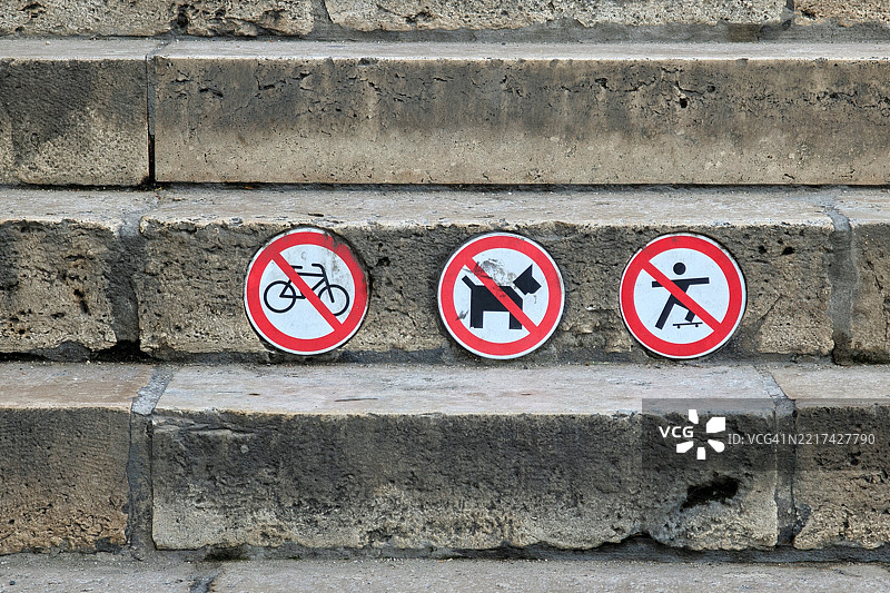 三个红色禁止标志位于混凝土台阶上，显示禁止骑自行车、禁止带狗和禁止滑板的符号，表示公共区域的限制。图片素材