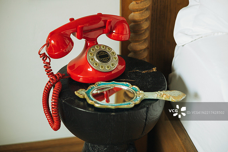 一部经典的红色电话和一面装饰镜子放在床头柜上。图片素材