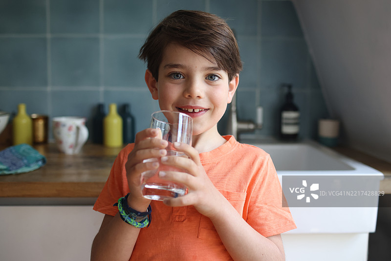 一个7岁男孩在厨房里喝水。图片素材
