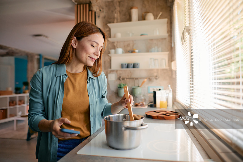 女性在现代厨房中使用智能手机和烹饪图片素材
