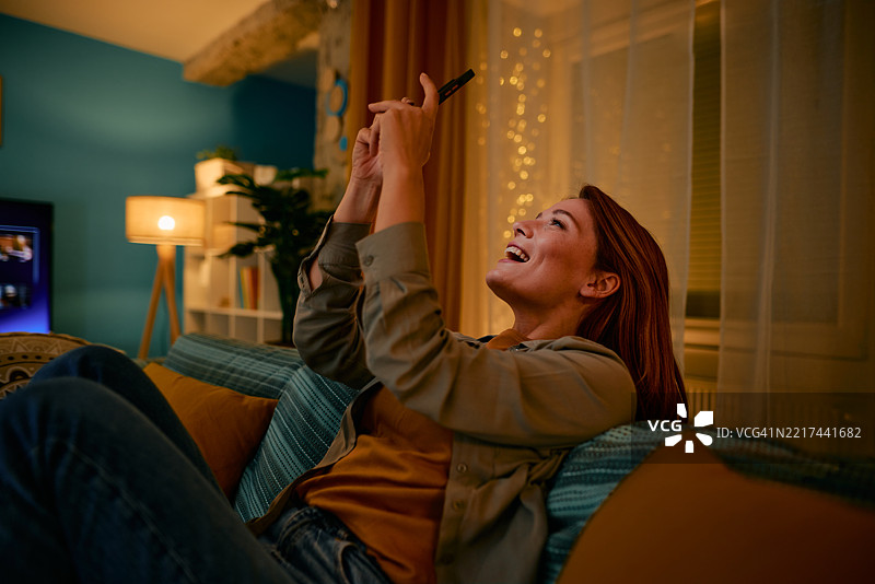 愉快的女性在家中沙发上放松时使用智能手机图片素材