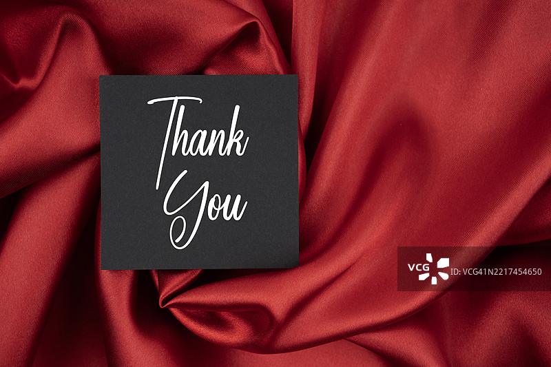黑色卡片上的金色“谢谢”字样，背景为红色缎带。图片素材