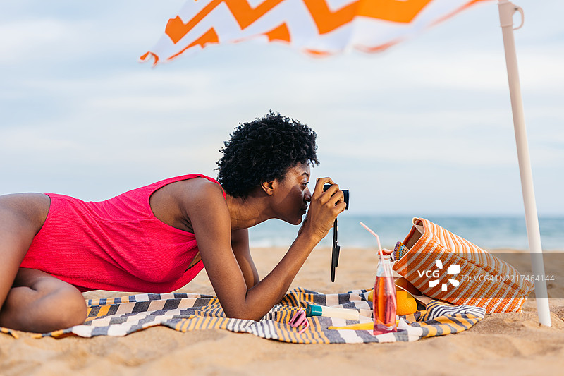 年轻的黑人女性在西班牙的海滩上放松时用相机拍照图片素材