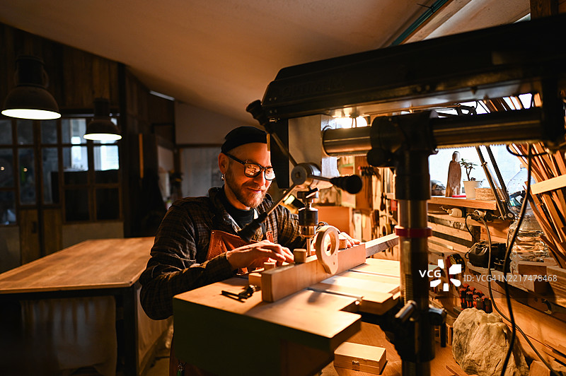 微笑的木匠在工作室里与木材一起工作图片素材