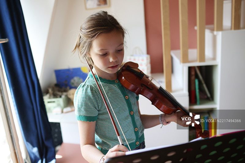 一个9岁女孩在她的卧室里拉小提琴图片素材