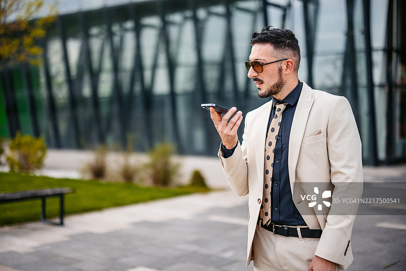 中年商人在公司大楼前用手机发送语音信息图片素材