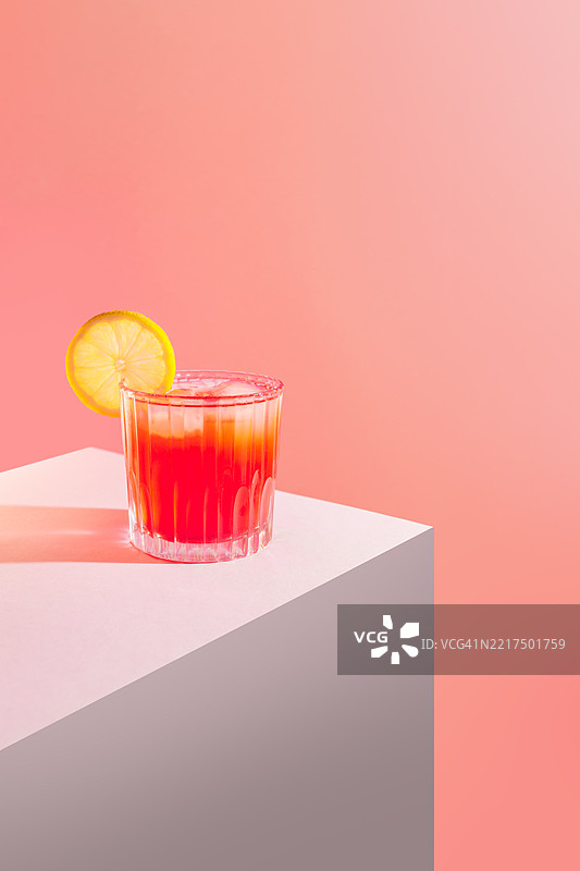 清新的红色鸡尾酒，配有柠檬片和冰块，背景为粉色图片素材