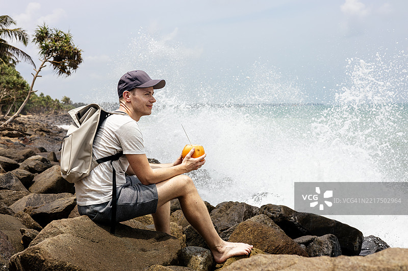 旅行者坐在海岸边，喝着椰子水图片素材