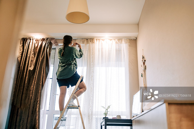 女人站在梯子上，在卧室里挂窗帘图片素材