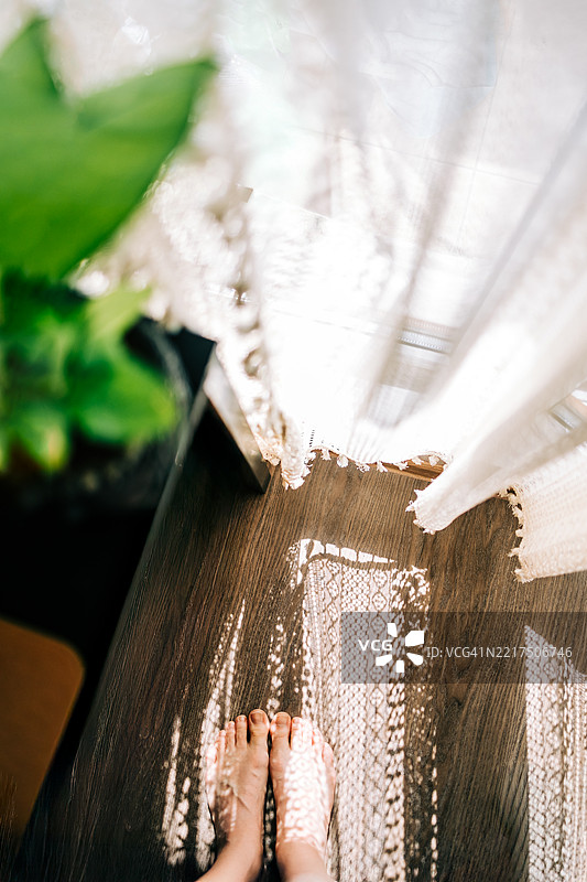 女人赤脚站在窗边，享受透过蕾丝窗帘洒进的阳光图片素材
