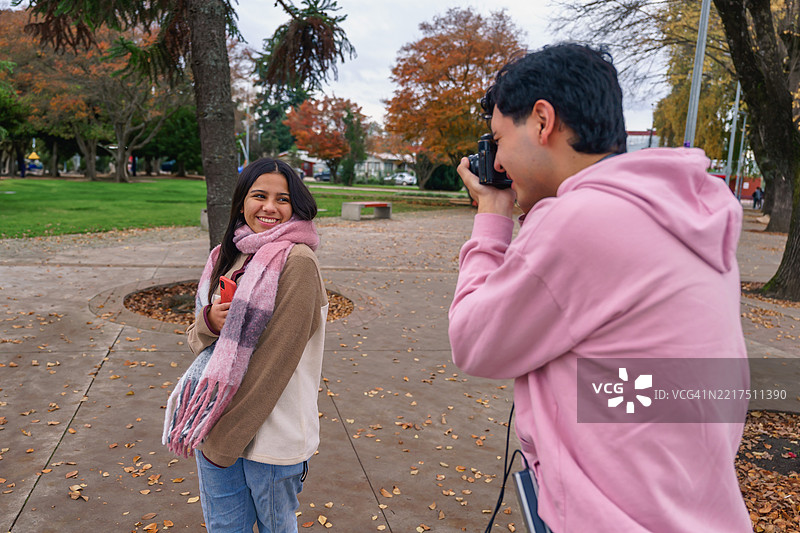 年轻男子在秋天的公园里用复古相机拍摄微笑的女友图片素材
